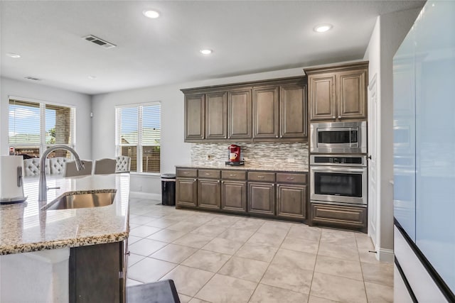 kitchen with sink, stainless steel appliances, light stone counters, light tile patterned flooring, and decorative backsplash