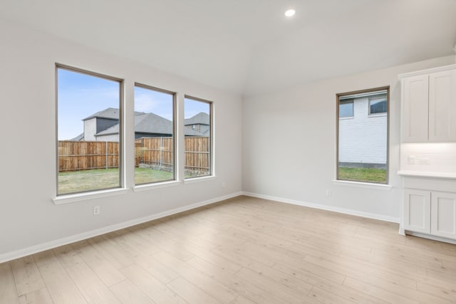 spare room with lofted ceiling, a wealth of natural light, and light wood-type flooring