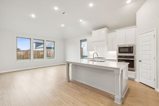 kitchen featuring built in microwave, sink, white cabinets, stainless steel oven, and a center island with sink