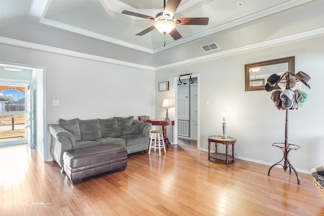 living room featuring a raised ceiling, ornamental molding, wood-type flooring, and ceiling fan