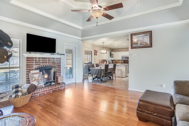 living room with crown molding, a healthy amount of sunlight, a brick fireplace, and light wood-type flooring