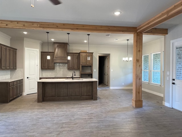 kitchen featuring a kitchen island with sink, hanging light fixtures, dark brown cabinets, custom exhaust hood, and beamed ceiling