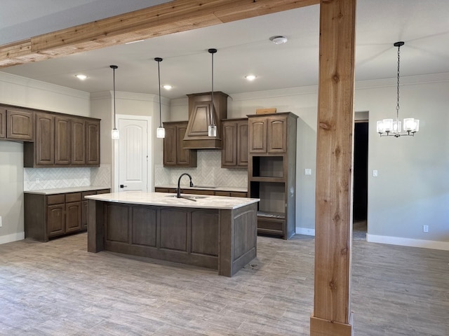 kitchen featuring custom exhaust hood, a kitchen island with sink, pendant lighting, and dark brown cabinetry