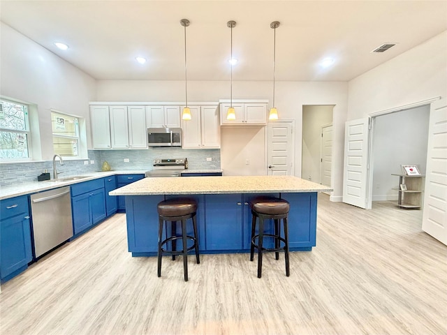 kitchen featuring a kitchen island, appliances with stainless steel finishes, white cabinets, and decorative light fixtures