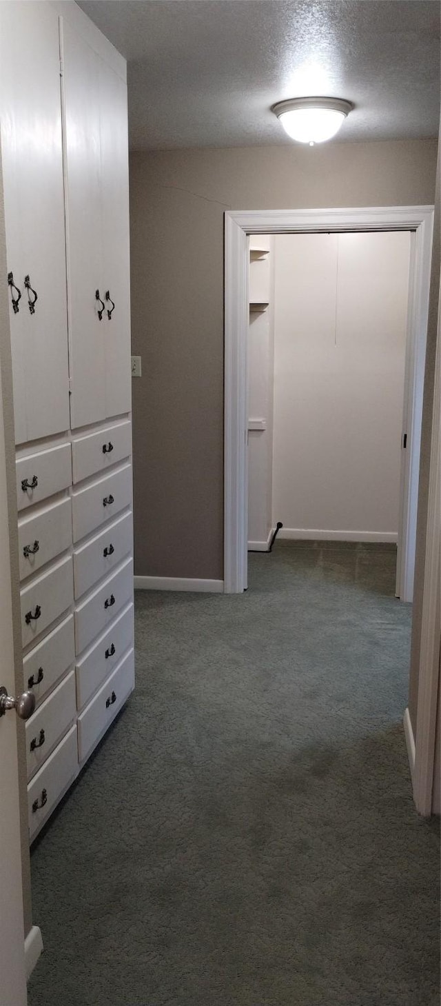 corridor featuring dark colored carpet and a textured ceiling