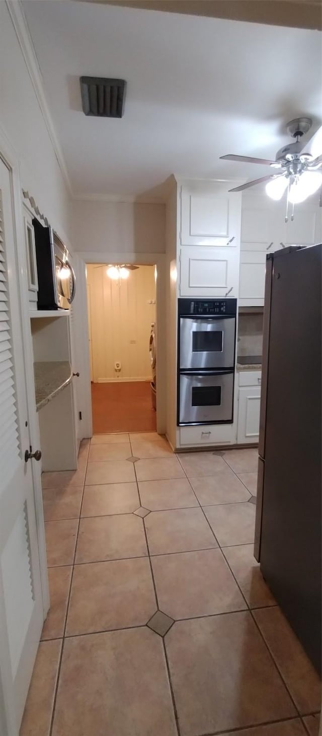 kitchen with white cabinets, light tile patterned floors, ceiling fan, stainless steel appliances, and crown molding