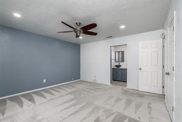 unfurnished bedroom featuring ceiling fan, light colored carpet, a textured ceiling, and ensuite bathroom