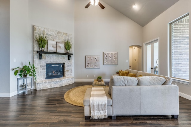 living room with dark hardwood / wood-style flooring, a stone fireplace, high vaulted ceiling, and ceiling fan