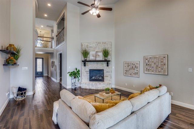 living room with a stone fireplace, dark hardwood / wood-style floors, ceiling fan, and a towering ceiling