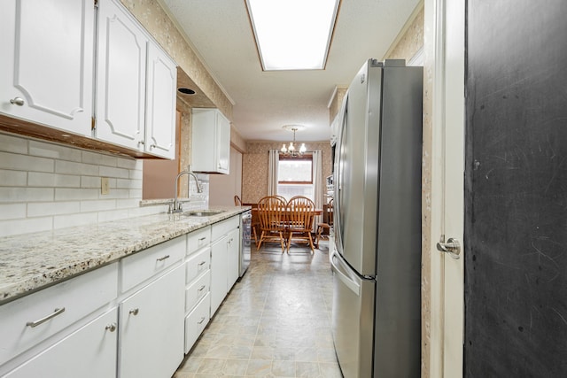 kitchen with sink, decorative light fixtures, stainless steel appliances, light stone countertops, and white cabinets