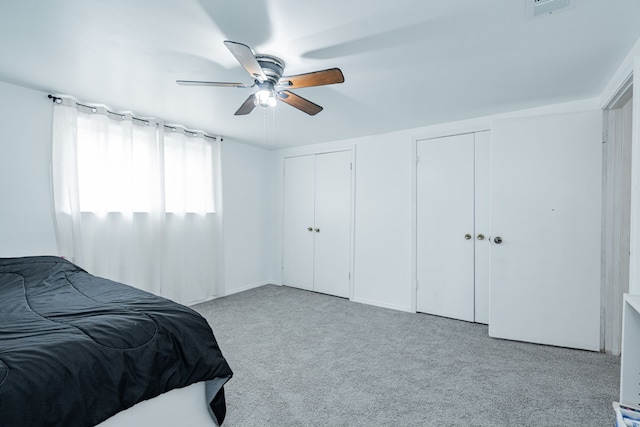 bedroom with multiple closets, light colored carpet, and ceiling fan