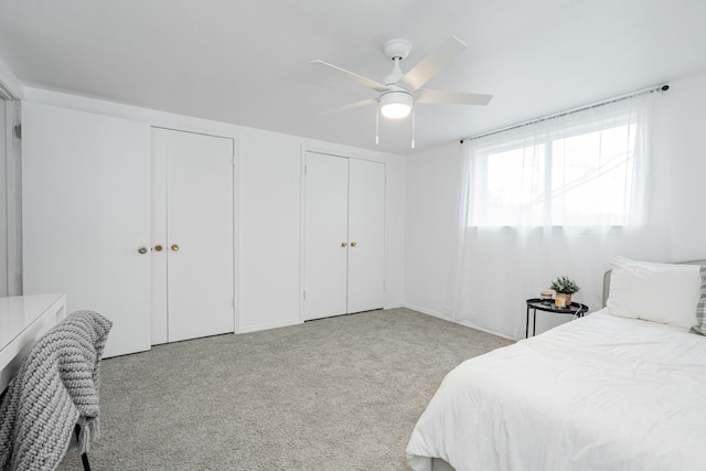 bedroom with ceiling fan, light colored carpet, and two closets