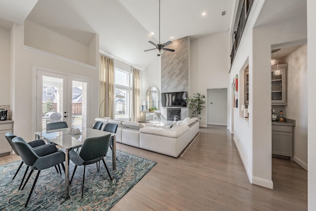 dining space with a fireplace, high vaulted ceiling, ceiling fan, light wood-type flooring, and french doors