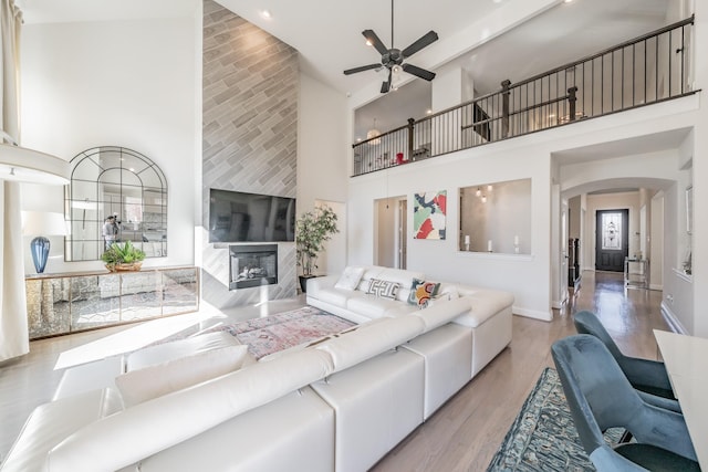 living room with light hardwood / wood-style flooring, a fireplace, ceiling fan, and a high ceiling