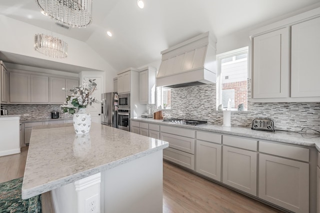 kitchen with premium range hood, lofted ceiling, a center island, appliances with stainless steel finishes, and gray cabinets