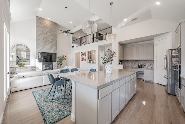 kitchen featuring a kitchen island, high vaulted ceiling, decorative light fixtures, light stone countertops, and light wood-type flooring