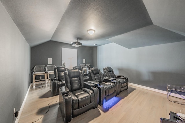 home theater room with lofted ceiling, hardwood / wood-style floors, and a textured ceiling