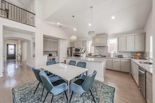 dining area featuring high vaulted ceiling, sink, and light hardwood / wood-style floors