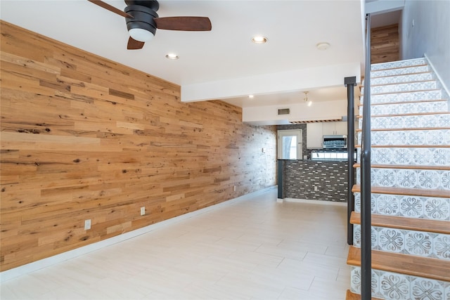 interior space with ceiling fan, beamed ceiling, and wood walls