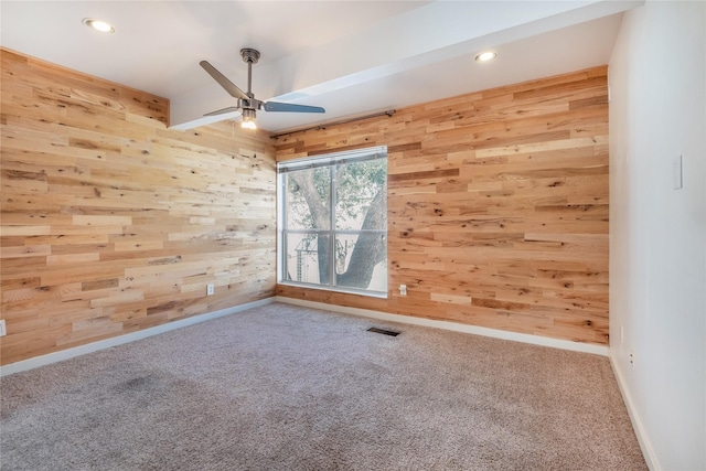 carpeted empty room with ceiling fan and wood walls