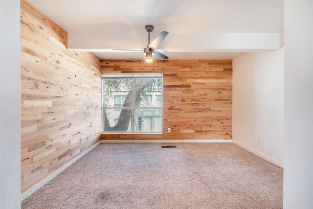 empty room with beamed ceiling, carpet, ceiling fan, and wood walls