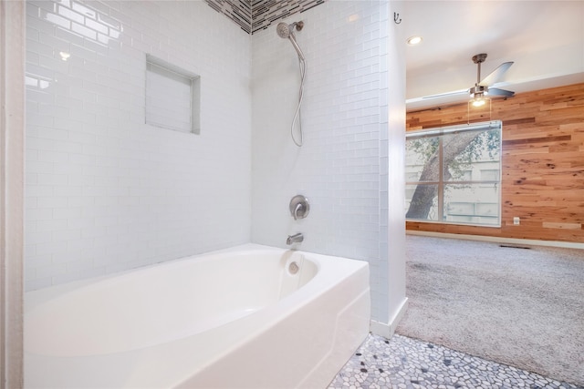 bathroom with tiled shower / bath combo, wooden walls, and ceiling fan