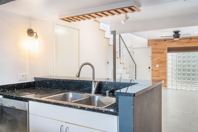 kitchen featuring sink, ceiling fan, wooden walls, white cabinets, and stainless steel dishwasher