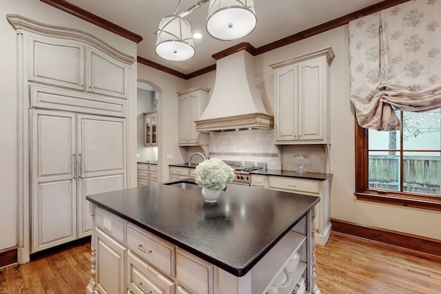 kitchen featuring pendant lighting, backsplash, ornamental molding, custom range hood, and light hardwood / wood-style flooring