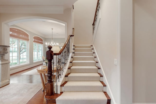 stairs featuring an inviting chandelier, hardwood / wood-style floors, and crown molding