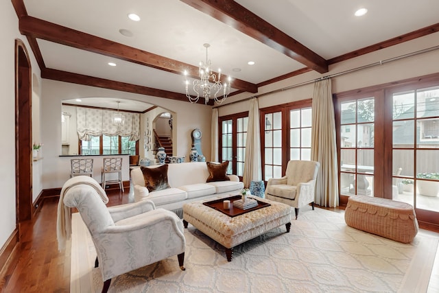 living room featuring beam ceiling, a healthy amount of sunlight, an inviting chandelier, and light hardwood / wood-style floors