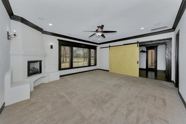 unfurnished living room featuring crown molding, a fireplace, a barn door, and carpet flooring