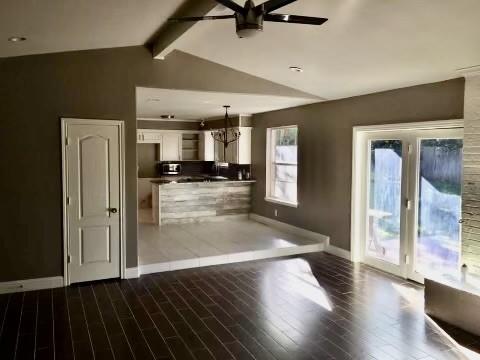 unfurnished living room with vaulted ceiling with beams, ceiling fan with notable chandelier, and hardwood / wood-style floors