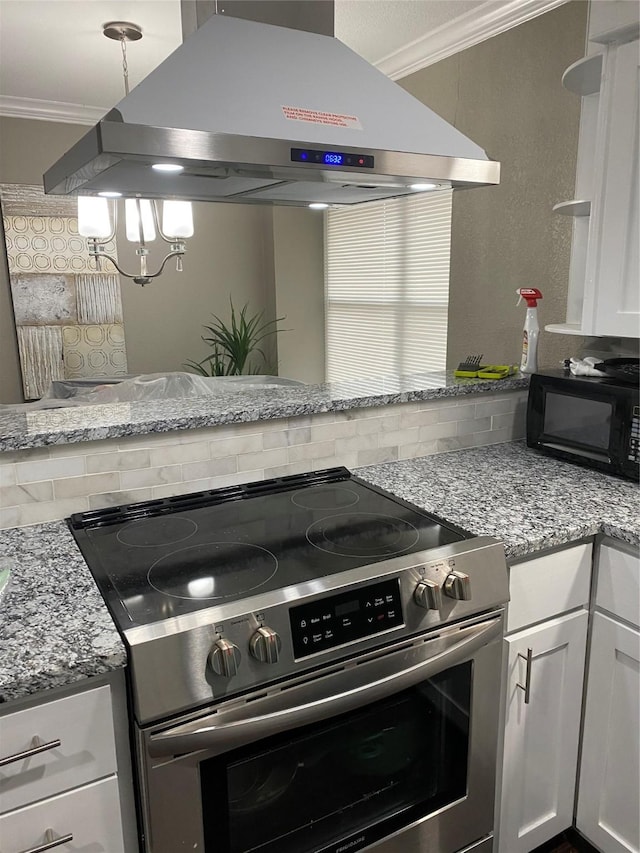 kitchen with light stone counters, island range hood, stainless steel electric range, ornamental molding, and white cabinets