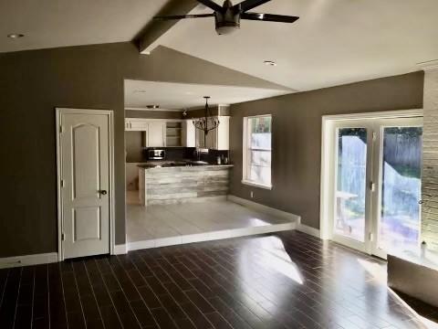 unfurnished living room with hardwood / wood-style floors, ceiling fan with notable chandelier, and lofted ceiling with beams