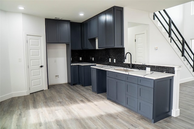 kitchen featuring tasteful backsplash, light stone countertops, sink, and light wood-type flooring