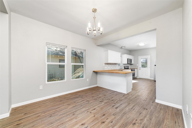 kitchen featuring a kitchen bar, butcher block counters, hanging light fixtures, kitchen peninsula, and white cabinets