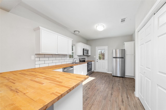 kitchen with butcher block countertops, white cabinetry, decorative backsplash, stainless steel appliances, and light hardwood / wood-style flooring