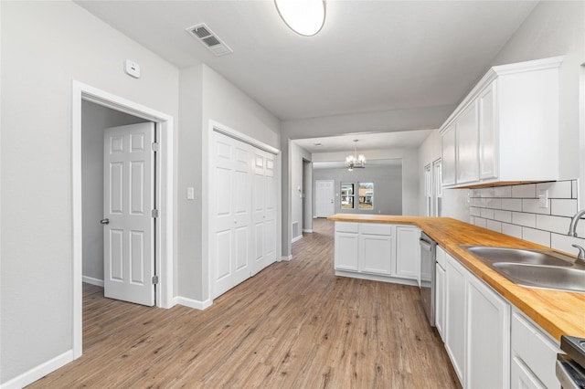 kitchen featuring pendant lighting, butcher block countertops, white cabinetry, sink, and stainless steel dishwasher