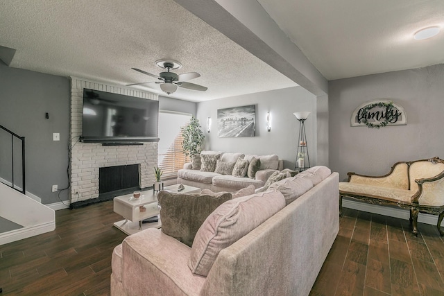 living room featuring a brick fireplace, dark wood-type flooring, a textured ceiling, and ceiling fan