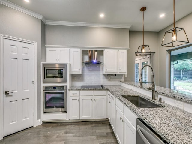 kitchen featuring wall chimney exhaust hood, sink, decorative light fixtures, stainless steel appliances, and white cabinets