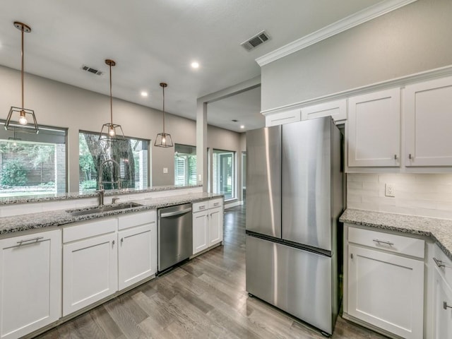 kitchen with sink, appliances with stainless steel finishes, white cabinetry, hanging light fixtures, and light stone countertops