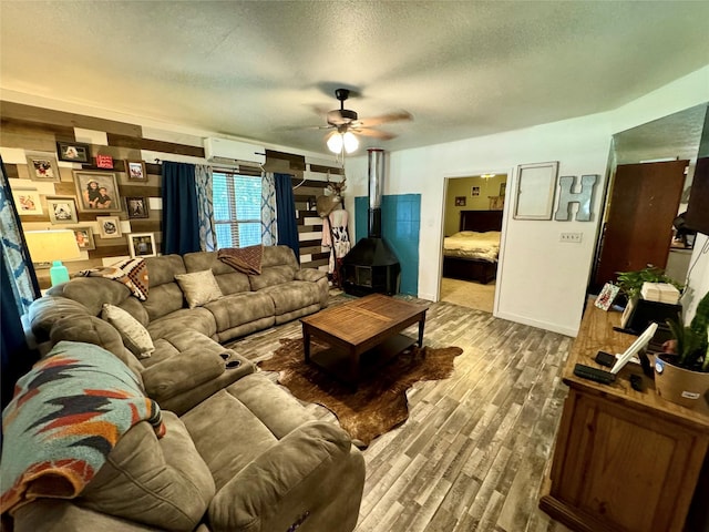 living room featuring a textured ceiling, a wood stove, a wall unit AC, ceiling fan, and hardwood / wood-style floors