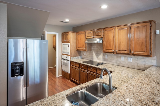 kitchen with sink, backsplash, light stone counters, light hardwood / wood-style floors, and white appliances