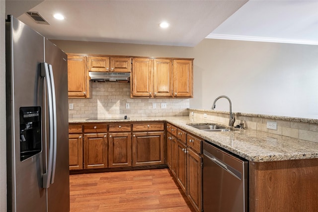 kitchen featuring appliances with stainless steel finishes, sink, light stone counters, kitchen peninsula, and light hardwood / wood-style flooring