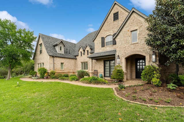 french country inspired facade with a front lawn, brick siding, french doors, and stone siding