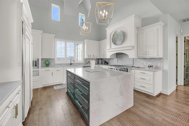 kitchen featuring stove, a sink, a kitchen island, white cabinetry, and pendant lighting