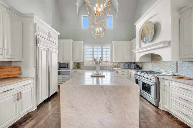 kitchen featuring built in appliances, white cabinets, a center island, decorative light fixtures, and an inviting chandelier