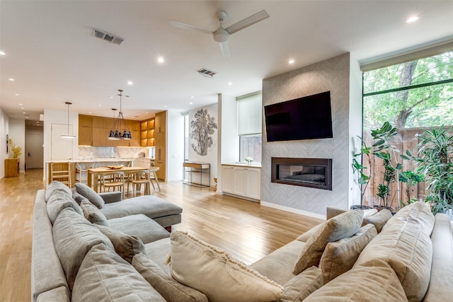 living room featuring ceiling fan, light hardwood / wood-style floors, and a tile fireplace