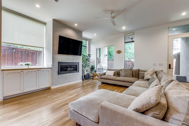 living room featuring ceiling fan, a large fireplace, and light hardwood / wood-style floors