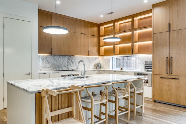 kitchen with decorative light fixtures, an island with sink, and stainless steel oven